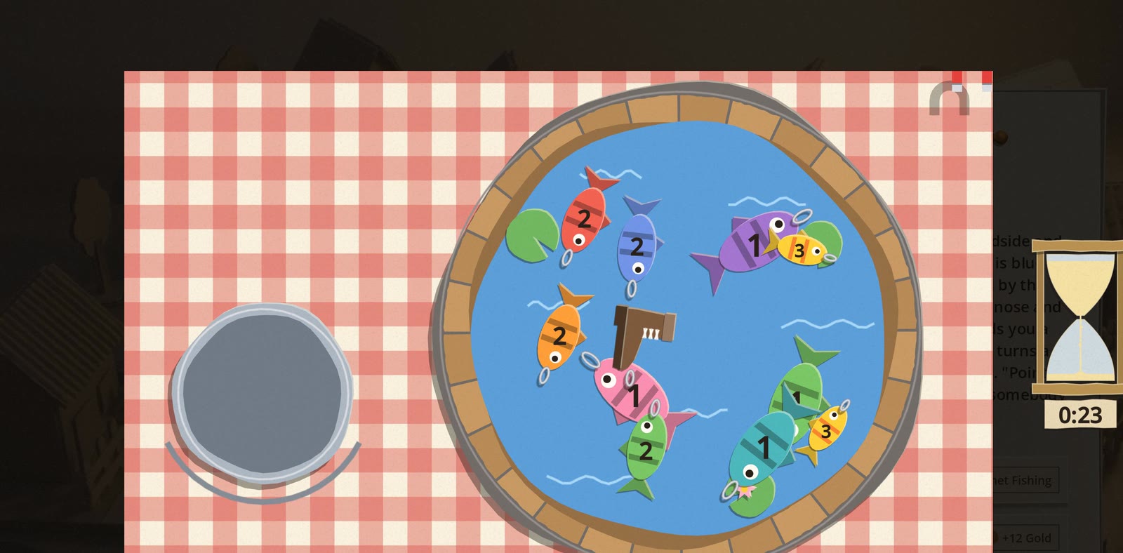 The Magnet Pond game: a round blue paper pond in a wooden tub on a red gingham cloth, full of card fish numbered 1 to 3, with a magnet on a line over them, an empty pail on the left and a sandglass at 0:23 on the right