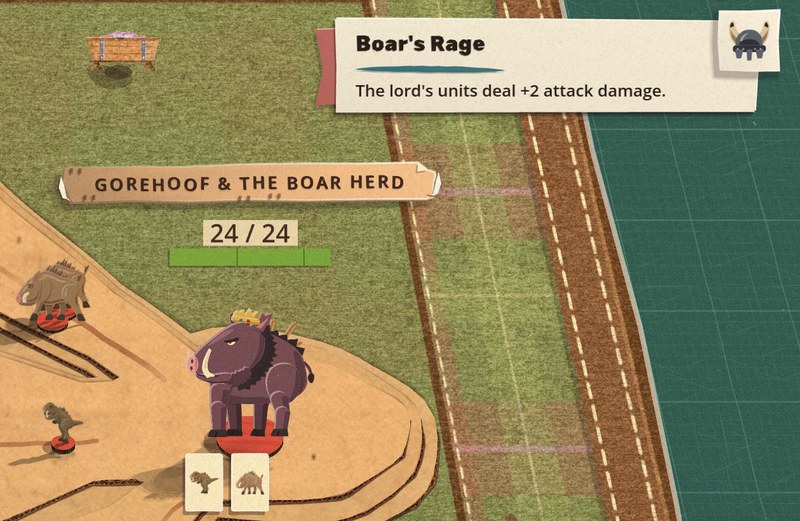 Top right of a fight against Gorehoof and the Boar Herd: the lord's power, Boar's Rage, is a cream paper slip on a red tab, its name in cut-paper letters, "The lord's units deal +2 attack damage." under it, and the power's punched counter, a horned helmet, laid on the slip's end