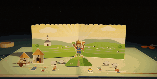 The crowned warlord stands on a green hill in front of a gold sunburst, with sheep grazing below and a white chapel in the distance. Villagers come out of their houses and gather at the foot of the hill