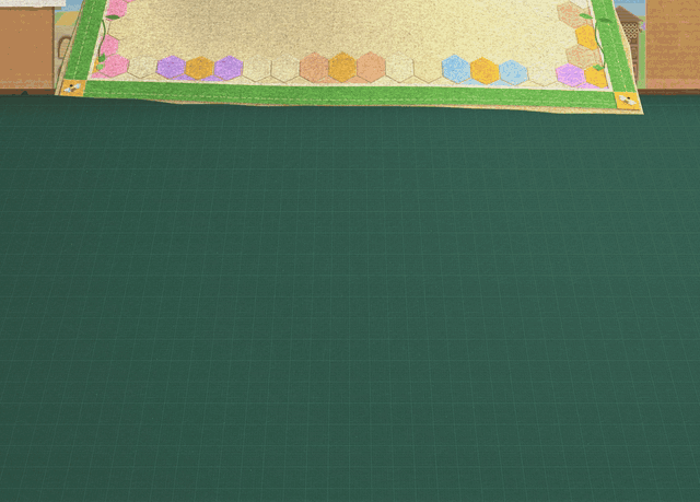 A cream mat bordered in green and pastel honeycomb cells floats down flat over the desk under Verdy B. Queen's wall, its edges slap down, and a pale blister of trapped air slides across under the felt and out at the side